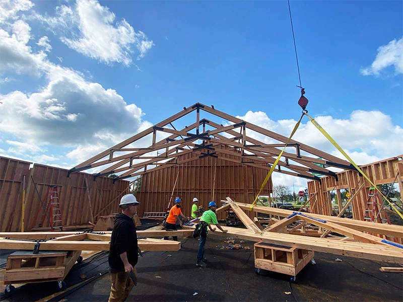 Construction workers lifting wood trusses onto a buildings frame