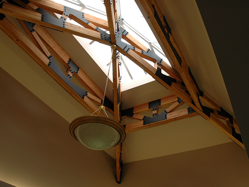 Image of wood beams and trusses underneath skylight window on ceiling.